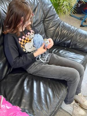 Ein Mädchen sitzt auf einem Sofa und macht aus einem Wollknäuel einen Pompon.