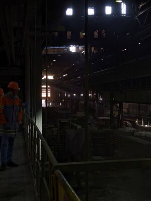 Über einen schmale Brücke geht die Schülergruppe an der großen Halle des Stahlwerks entlang.