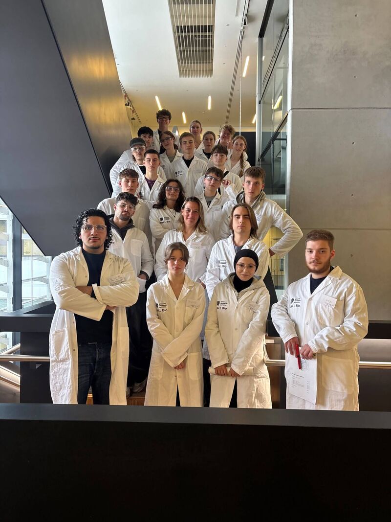 Die Bio-Kurse der Q 1 haben sich in weißen Kitteln zu einem Gruppenfoto auf einer Treppe aufgestellt.
