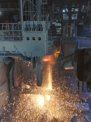 Aus einem großen Container wird Schrott in die Stahlpfanne gekippt. Dabei entstehen viele Funken.