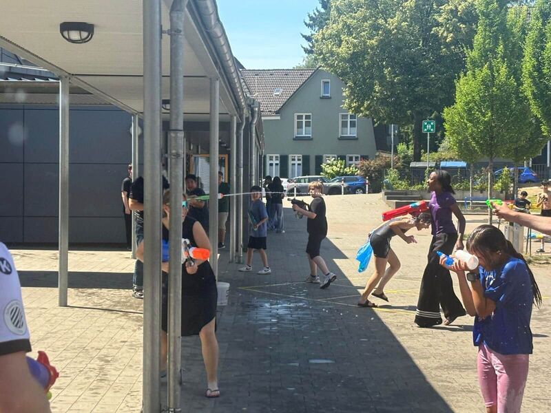 Auf dem Schulhof laufen Kinder und eine Lehrerin durcheinander und beschießen sich mit Wasserpistolen. Wer ist am nassesten?