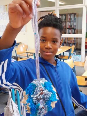 Ein Junge präsentiert stolz seinen gerade erstellten bunten Pompom.