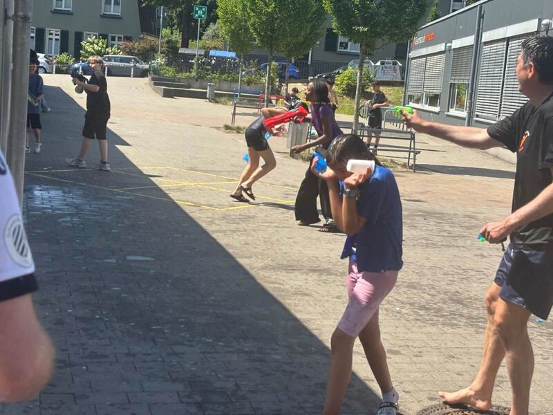 Auf dem Schulhof laufen Kinder und der Schulleiter durcheinander und beschießen sich mit Wasserpistolen. Wer ist am nassesten?