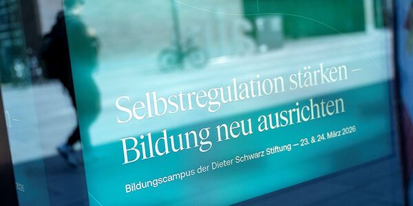 In einer Glasscheibe spiegelt sich das Plakat des Kongresses Selbstregulation stärken