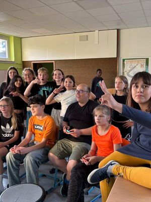 Drei Schüler:innen und ein Lehrer werden beim Mario-Kart-Spielen von anderen angefeuert.