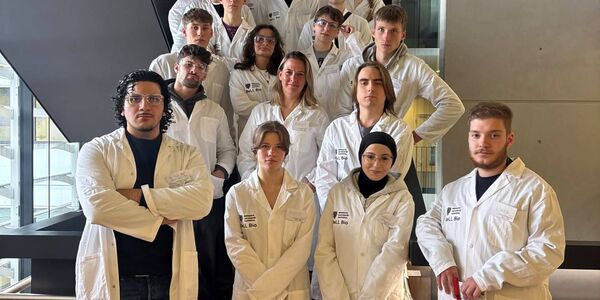 Die Bio-Kurse der Q 1 haben sich in weißen Kitteln zu einem Gruppenfoto auf einer Treppe aufgestellt.