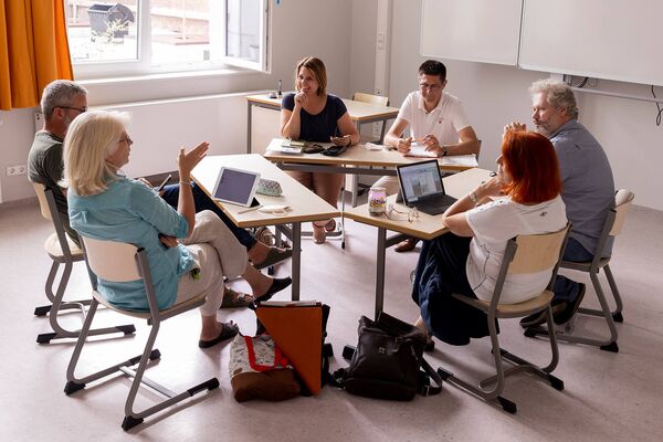 Personen sitzen in einem Tischkreis zusammen und tauschen sich über unterschiedliche Ideen aus. Personen sitzen in einem Tischkreis zusammen und tauschen sich über unterschiedliche Ideen aus.
