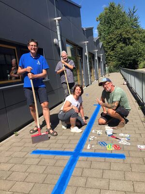 Eine Gruppe von Lehrkräften ist gerade dabei einen blauen Zahlenstrahl auf den Schulhof zu malen.