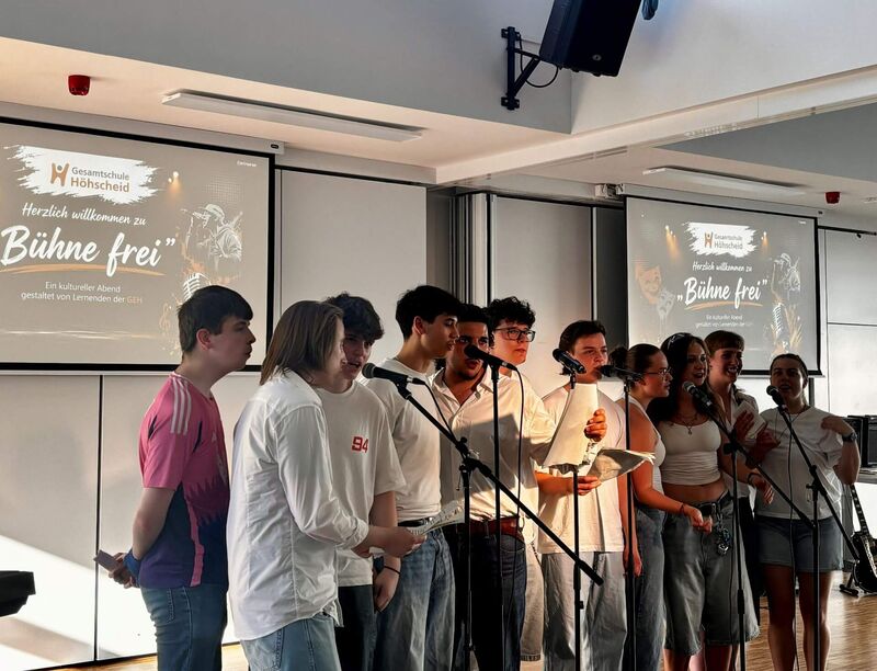 Der Vokalpraktische Kurs hat sich in einer Reihe aufgebaut und steht an den Mikrofonen. In einigen Gesichtern ist der Spaß am Singen zu sehen. Andere kommen noch nicht so aus sich heraus.