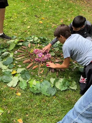 Schülerinnen und Schüler erstellen mit gefundenen Gegenständen eine geometrische Form auf einer Wiese.