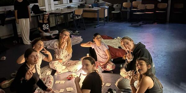 In der Klasse, wo die Mädchen geschlafen haben, sitzen sieben sechs Mädchen und eine Sozialpädagogin im Kreis und spielen im Schein einer Nachtlampe Karten.