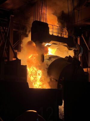 Aus der Stahlpfanne wird der flüssige Stahl ausgeschüttet. Dabei entstehen große Flammen und Rauch.