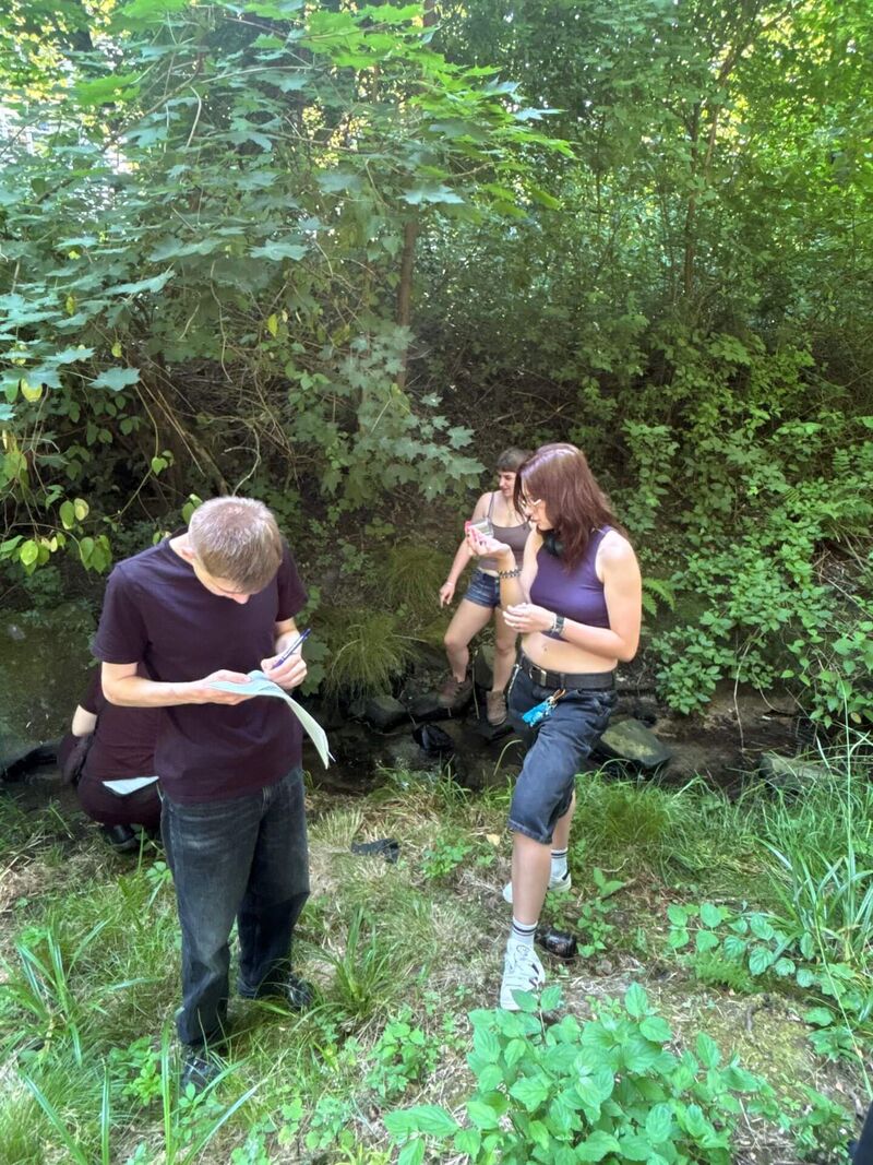 Drei Schüler:innen haben Tiere am Bach gefangen und notieren deren Name in ein Protokoll.